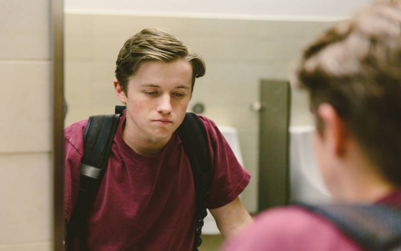 A depressed teen looking in the mirror at a school bathroom.