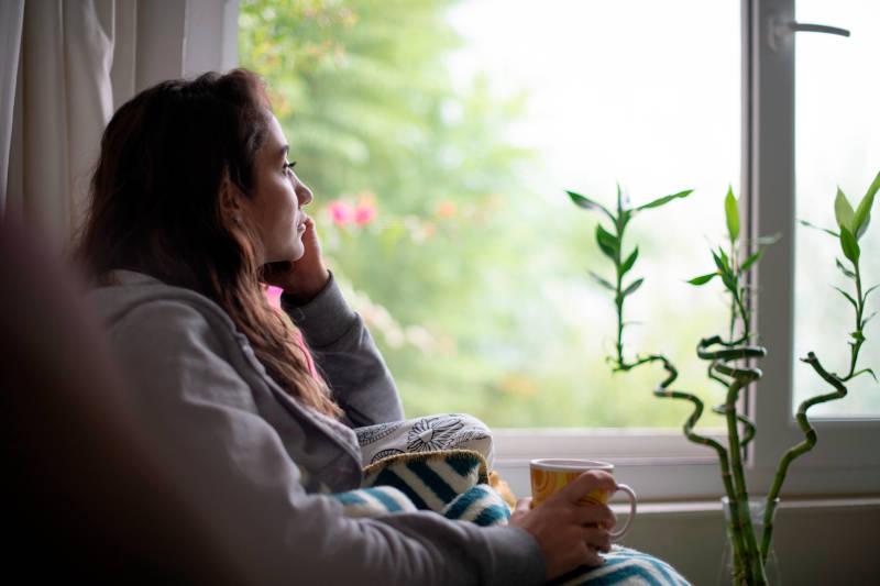 A sad woman looking out a window, experiencing bipolar disorder or depression.